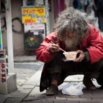 A homeless man in the back streets of Shibuya tucking in to a bowl of noodles